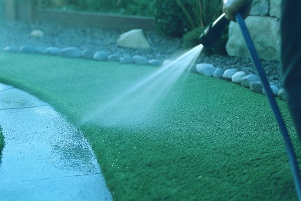 Person using a hose to rinse debris off an artificial lawn