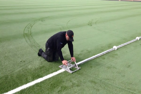 A close-up of a Line Cutter tool making a straight cut on the back of an artificial turf roll