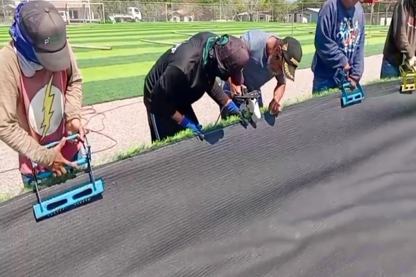 Two workers using Grass Grip tools to pull two large pieces of artificial turf together