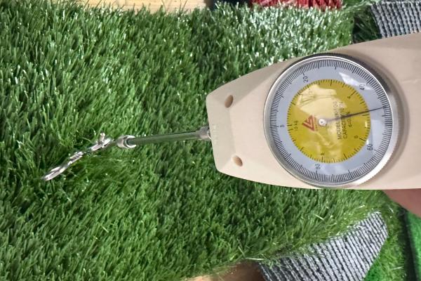 A person's hands testing the yarn pull-out strength of an artificial grass sample