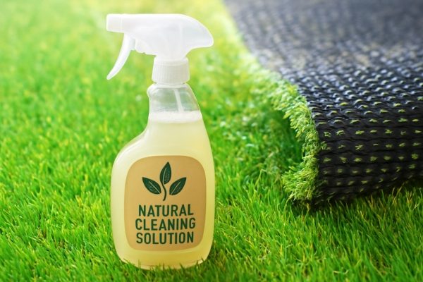 A spray bottle with a natural cleaning solution on a lush artificial lawn