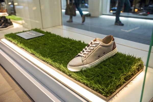 Close-up of a shoe displayed on a patch of artificial grass in a brightly lit shop window