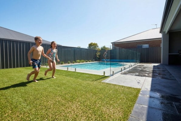 Children playing on cool artificial grass next to a pool
