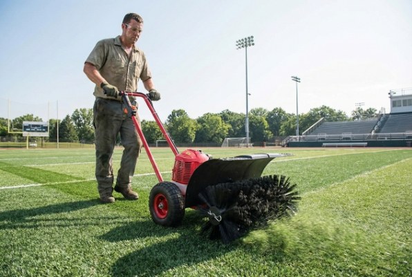Worker operating an artificial grass brushing machine on a sports field