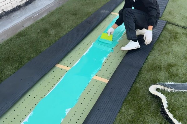worker applying two-component glue to artificial turf seams